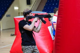 Боец LASERWAR наводит прицел на противника у красного укрытия.
